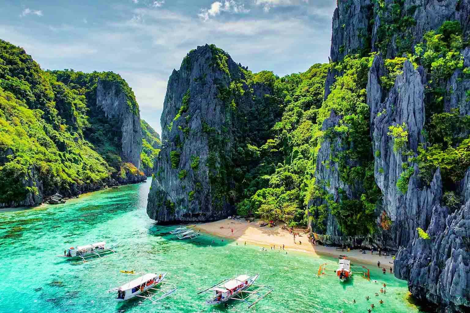 Philippines Visa Limestone cliffs surrounding turquoise lagoon with traditional boats and sandy beach in El Nido, Philippines